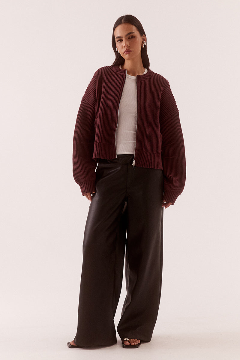 Model wearing a fully fashioned knit bomber cardigan with dropped shoulders, wide sleeves, ribbed trims, silver front zipper and welt pockets.