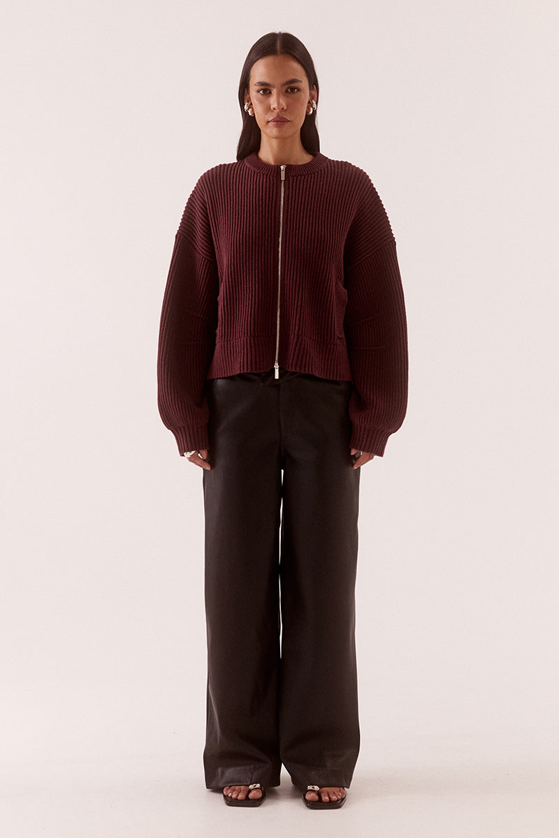 Model wearing a fully fashioned knit bomber cardigan with dropped shoulders, wide sleeves, ribbed trims, silver front zipper and welt pockets.