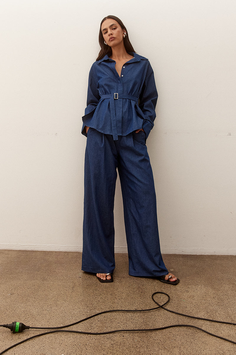 Model wearing an oversized cotton long sleeve shirt with dropped shoulders, wide cuffs, concealed buttons and side seam fixed fabric belt.