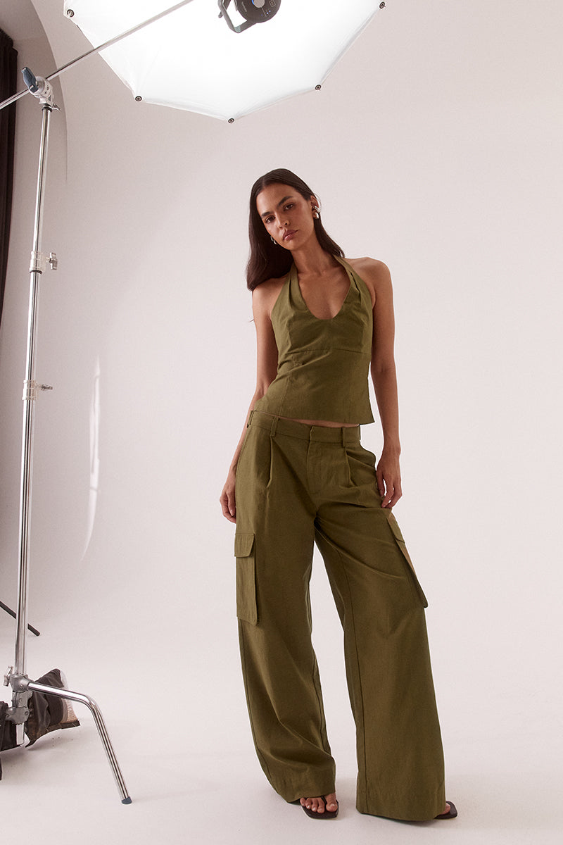 Model wearing a Lyocell cotton blend halter neck top featuring a scoop neckline, pleated detailing around the neckline, empire and body seams for shaping, adjustable button-back closure, side shirring, and a fitted lined bodice.