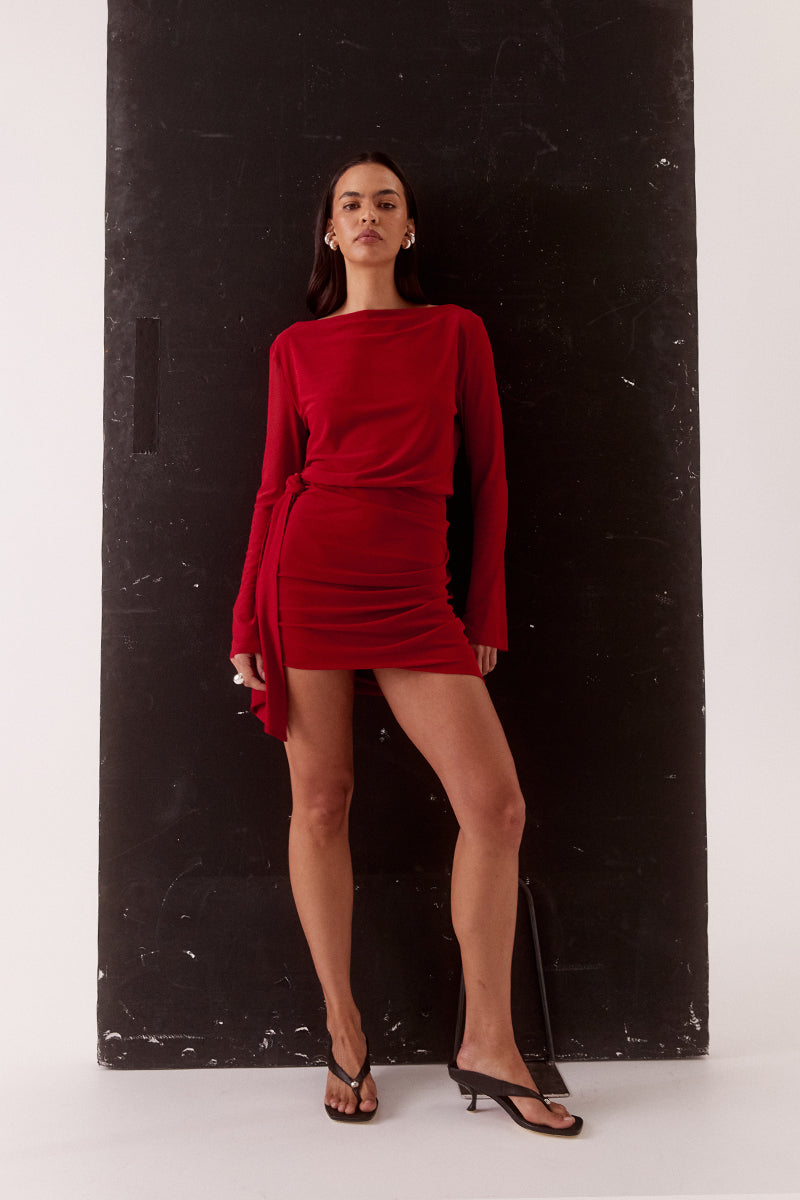 Model wearing a stretch mesh mini dress with boat neckline, long sleeves, elasticated waist, hip tuck detailing and asymmetric bubble hem skirt.