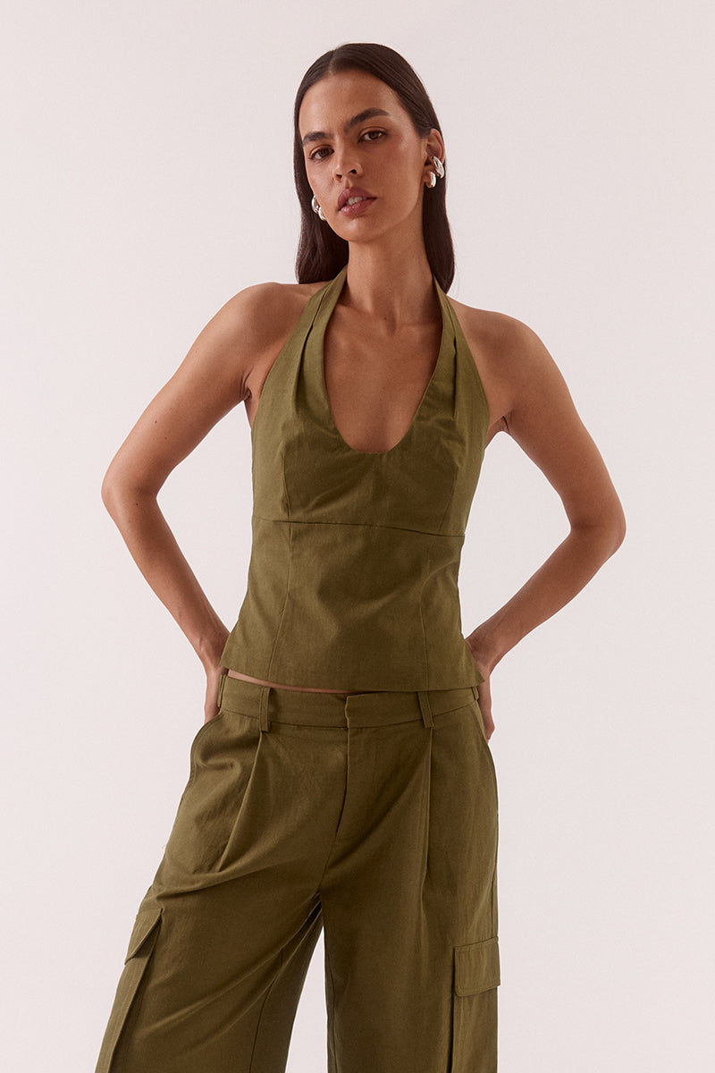 Model wearing a Lyocell cotton blend halter neck top featuring a scoop neckline, pleated detailing around the neckline, empire and body seams for shaping, adjustable button-back closure, side shirring, and a fitted lined bodice.
