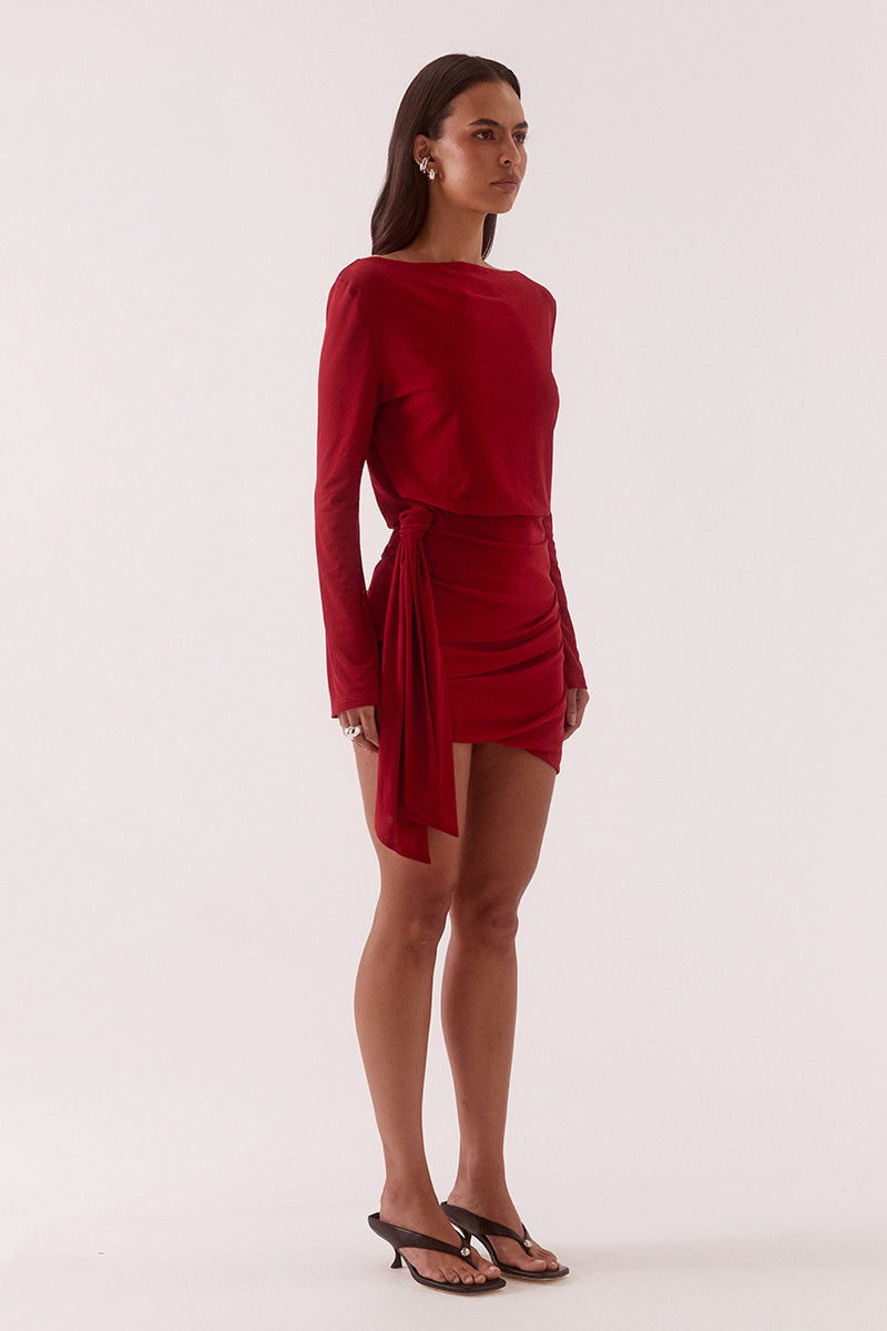 Model wearing a stretch mesh mini dress with boat neckline, long sleeves, elasticated waist, hip tuck detailing and asymmetric bubble hem skirt.