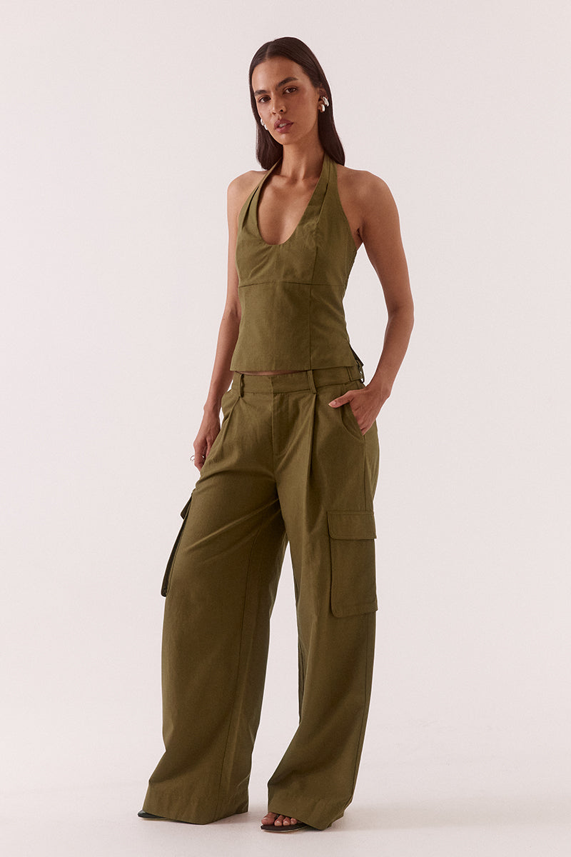 Model wearing a Lyocell cotton blend halter neck top featuring a scoop neckline, pleated detailing around the neckline, empire and body seams for shaping, adjustable button-back closure, side shirring, and a fitted lined bodice.