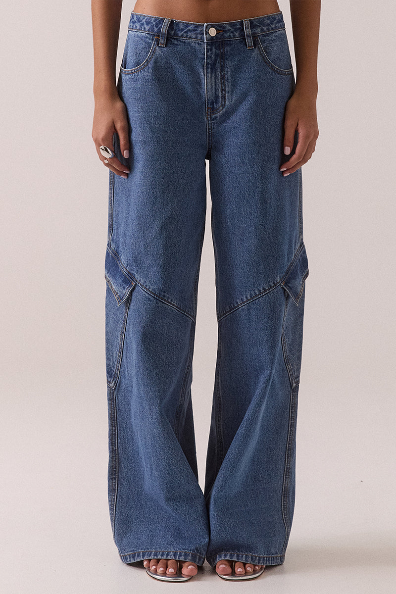 Model wearing mid rise wide leg cargo pants in vintage stone wash cotton with functional front, back and leg patch pockets and relaxed structured fit.