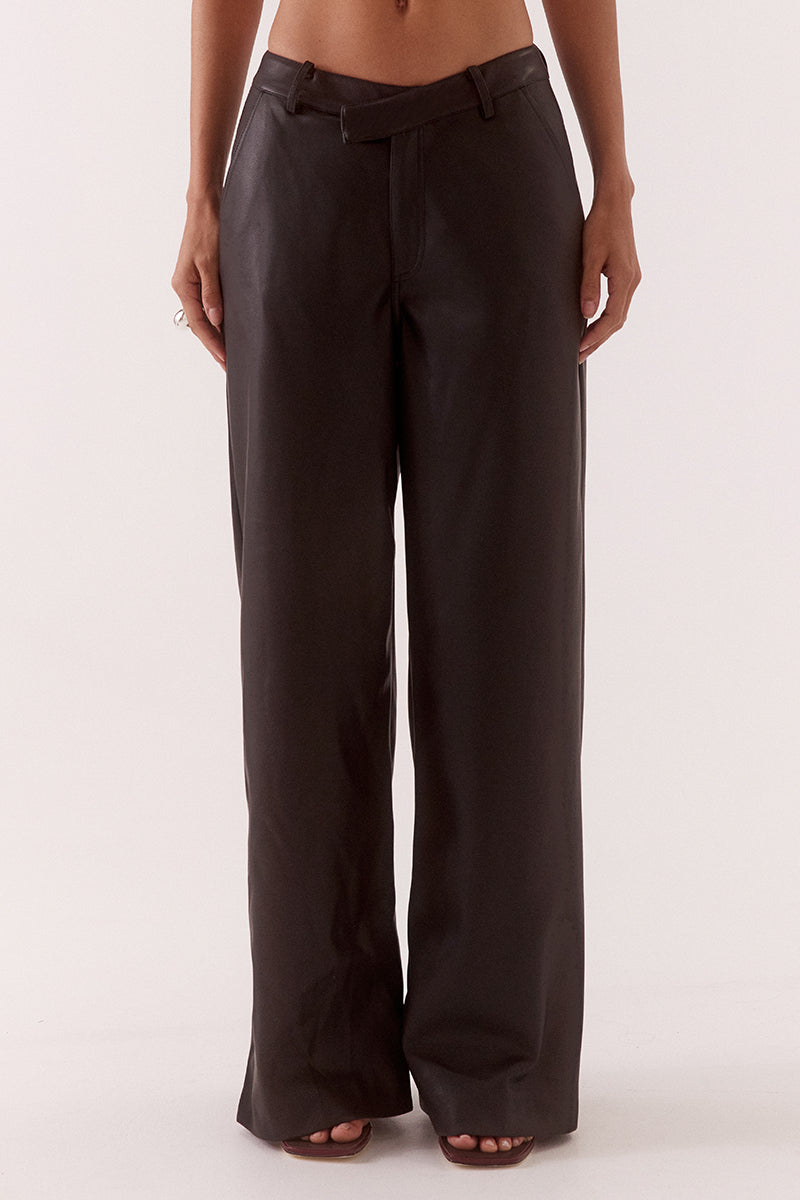 Model wearing black faux leather wide leg pants with angled waistband, fly front closure, and functional pockets, styled in a high-waisted tailored fit.