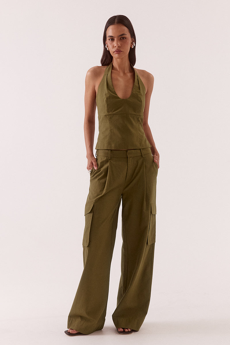 Model wearing a Lyocell cotton blend halter neck top featuring a scoop neckline, pleated detailing around the neckline, empire and body seams for shaping, adjustable button-back closure, side shirring, and a fitted lined bodice.