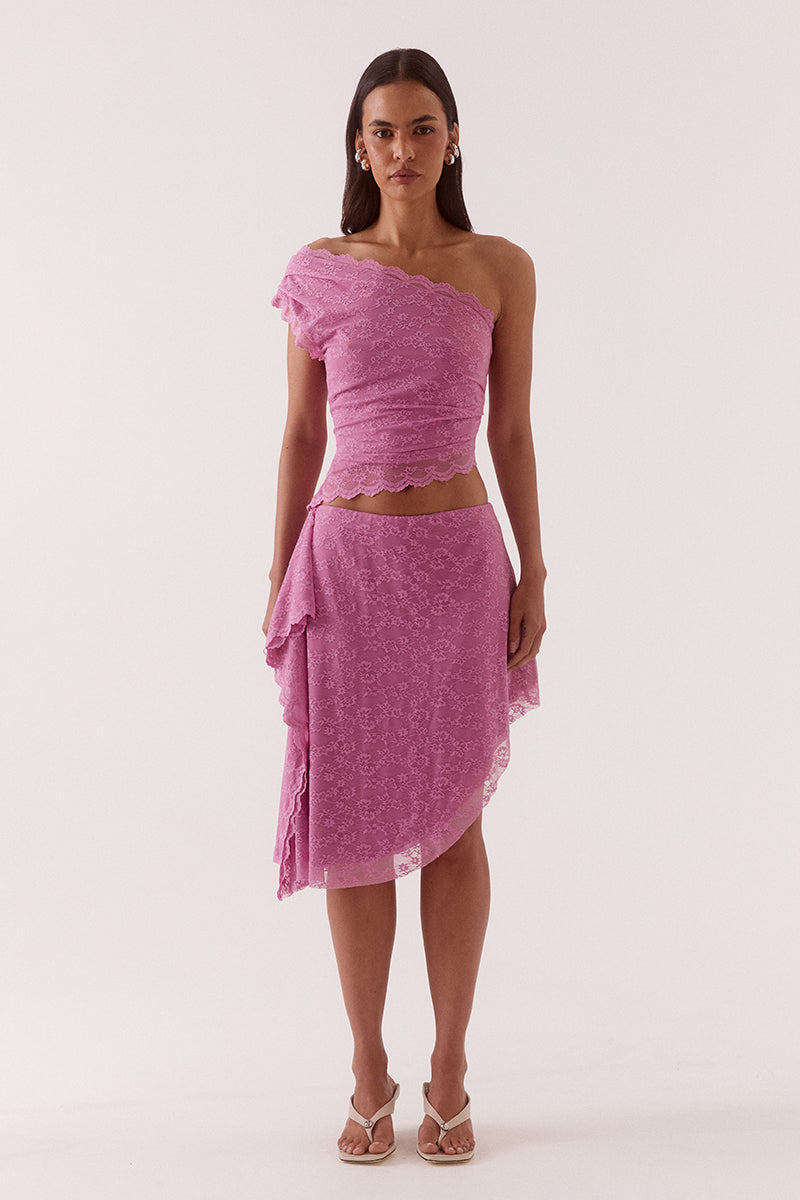 Model wearing a stretch lace mid rise skirt with an asymmetric hem, waterfall side drape panel and scalloped edge detailing.