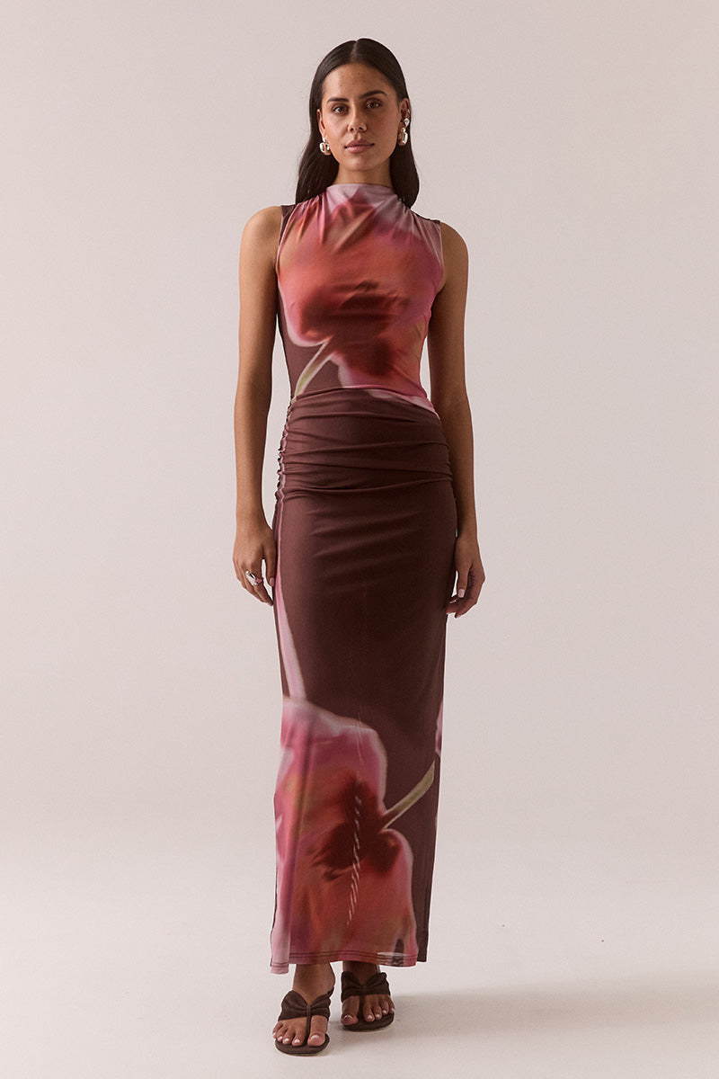 Model wearing exclusive print fitted maxi dress in stretch mesh with funnel neckline, gathered shoulders and hips, back cut-out detail, hem split, and fully lined contour fit.