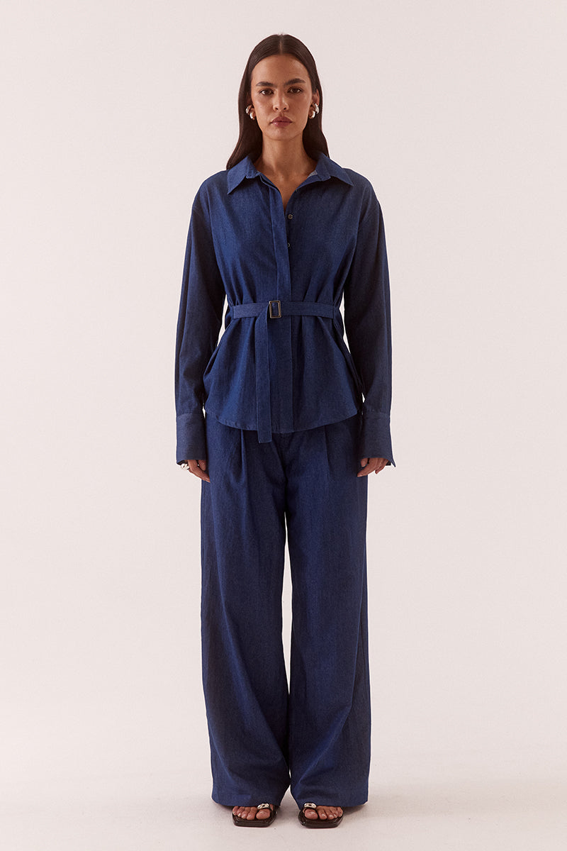 Model wearing an oversized cotton long sleeve shirt with dropped shoulders, wide cuffs, concealed buttons and side seam fixed fabric belt.