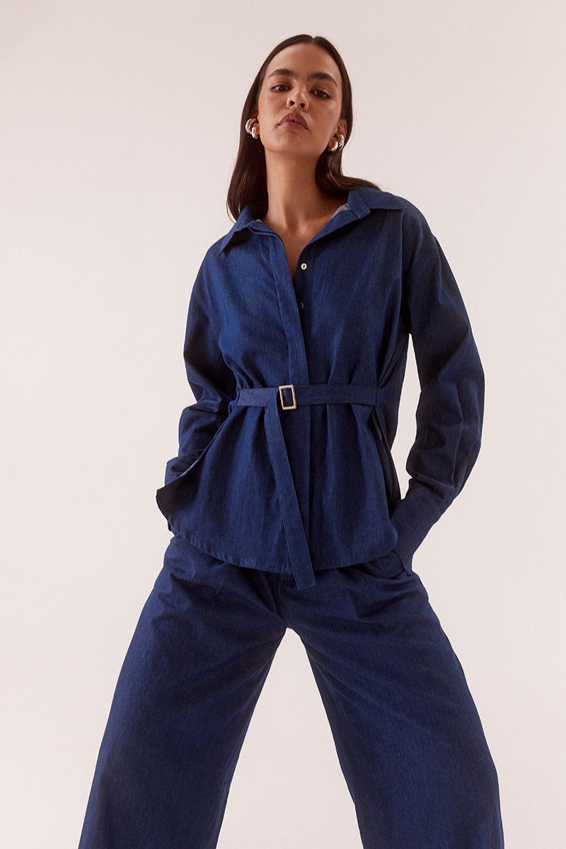 Model wearing an oversized cotton long sleeve shirt with dropped shoulders, wide cuffs, concealed buttons and side seam fixed fabric belt.