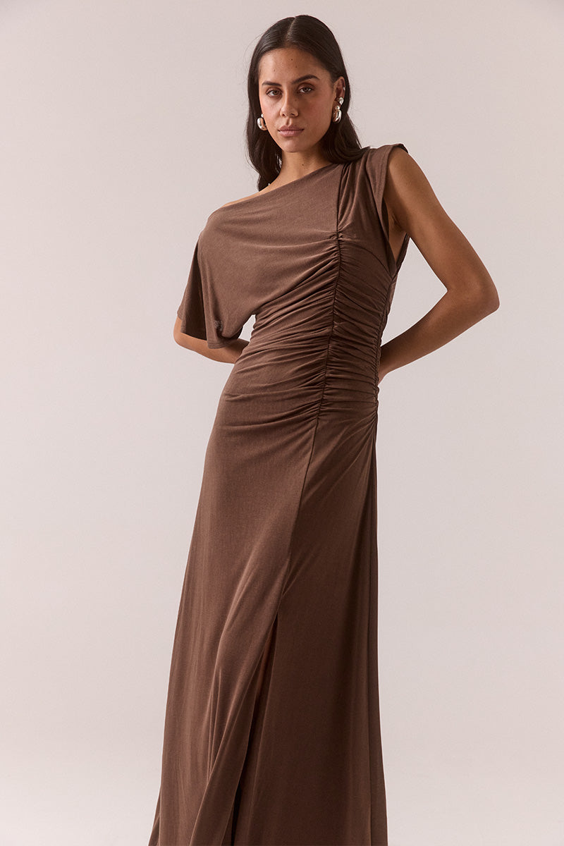 Model wearing slinky modal blend maxi dress with off-shoulder neckline option, asymmetric sleeve with split detail, gathered side seam, front hem split, and fully lined body-skimming silhouette.