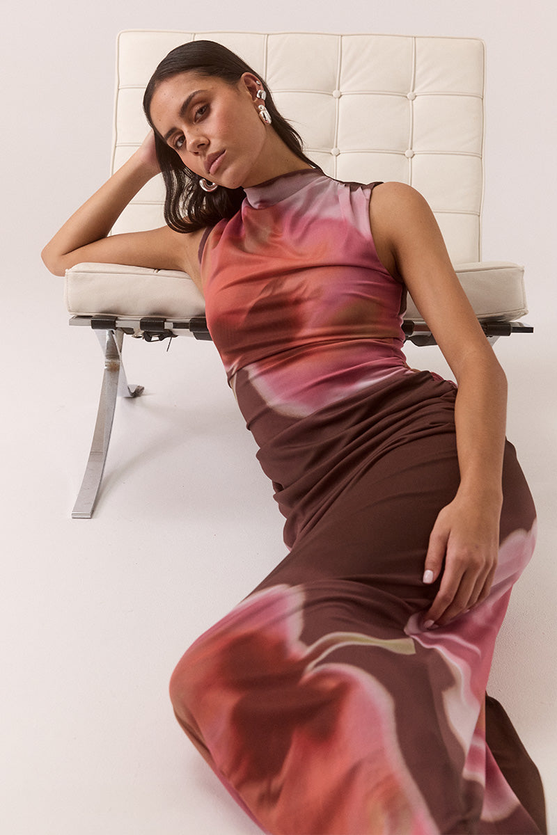 Model wearing exclusive print fitted maxi dress in stretch mesh with funnel neckline, gathered shoulders and hips, back cut-out detail, hem split, and fully lined contour fit.