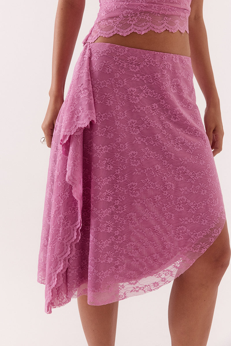 Model wearing a stretch lace mid rise skirt with an asymmetric hem, waterfall side drape panel and scalloped edge detailing.