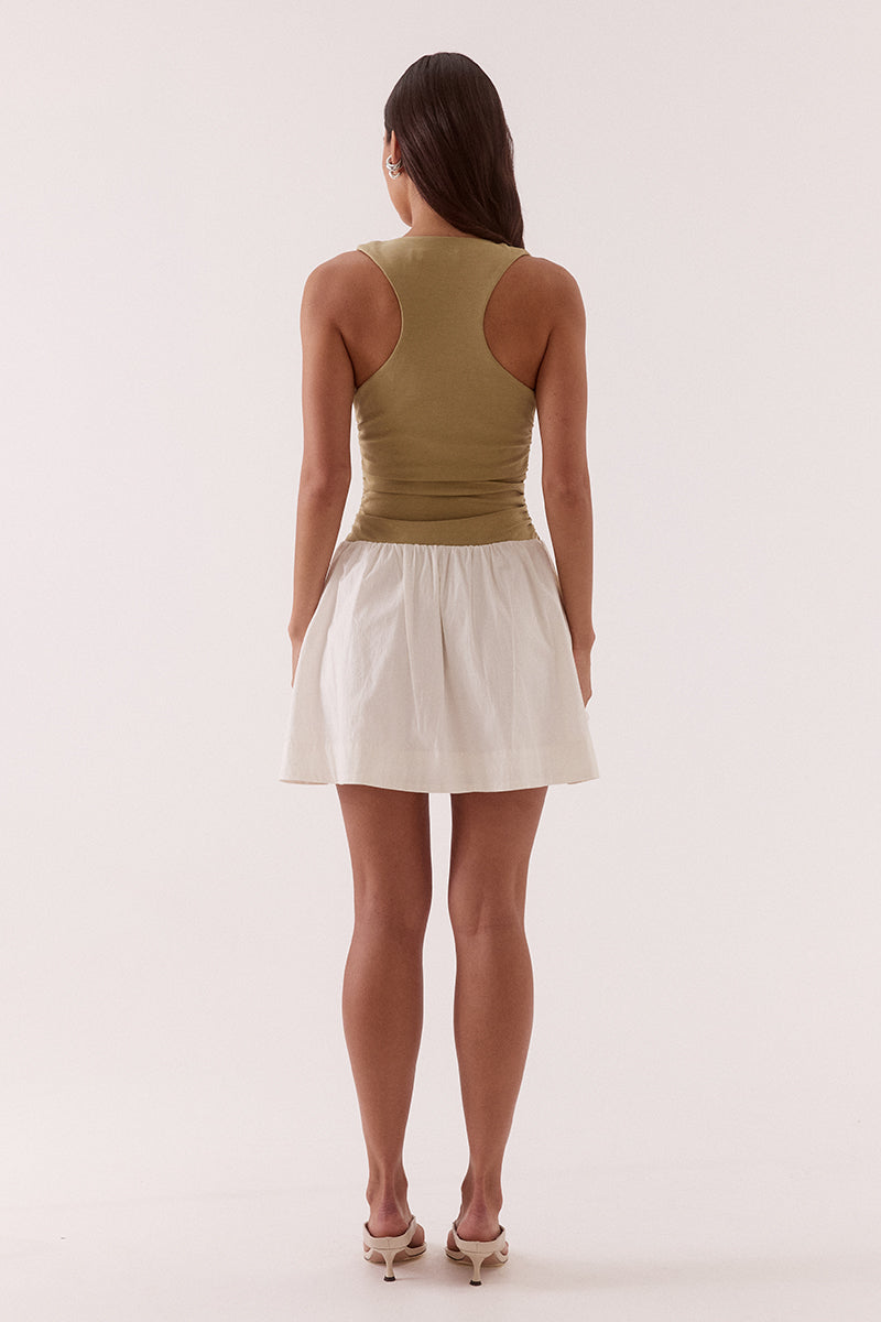 Model wearing a mixed fabric mini dress with a stretchy sleeveless bodice, deep scoop neckline with adjustable drawstring, racer back, gathered detailing through the bodice and skirt, side pockets, and a fully lined silhouette.