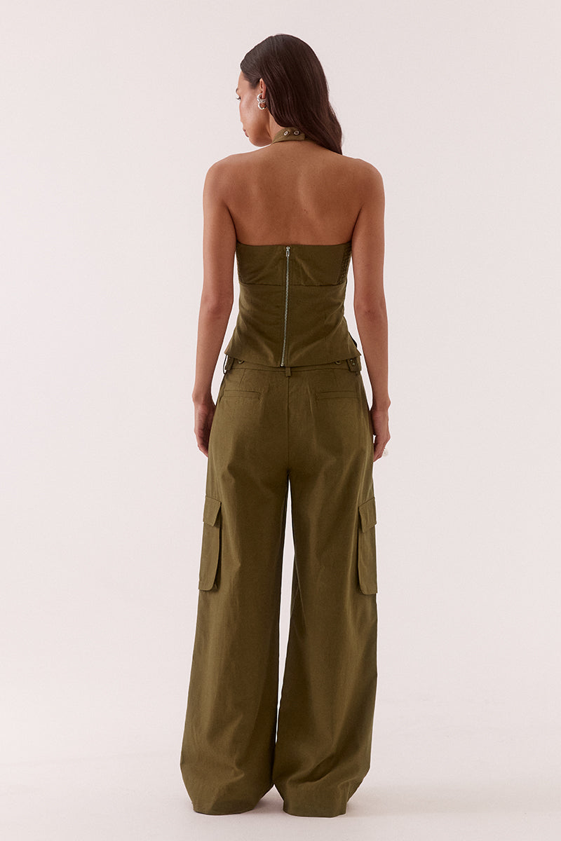 Model wearing a Lyocell cotton blend halter neck top featuring a scoop neckline, pleated detailing around the neckline, empire and body seams for shaping, adjustable button-back closure, side shirring, and a fitted lined bodice.